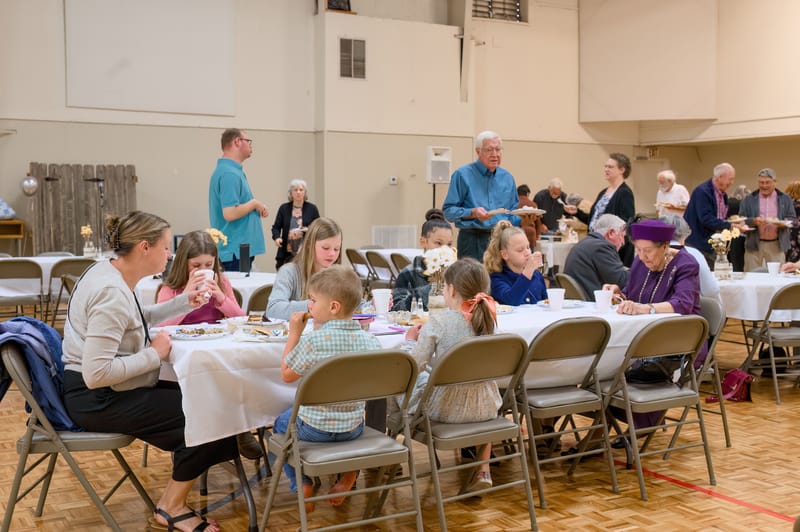 Children and adults seated together at a round table during a church fellowship meal.