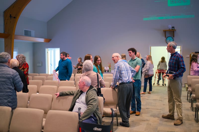Church members greeting one another among the rows of sanctuary chairs.
